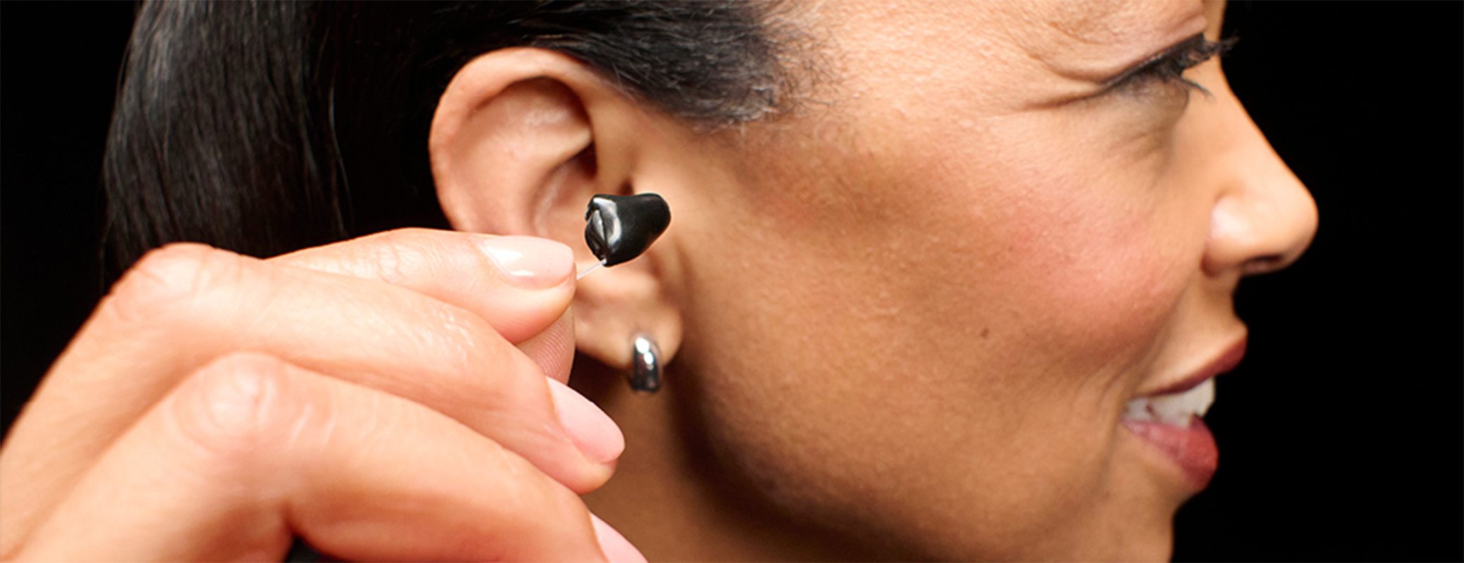 Image of a middle aged woman ready to insert a custom Omega AI Plus hearing aid